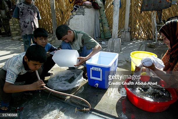 Gypsy boys drink from a tap as their mother washes clothes in their family home in a former Air Force base on November 14, 2004 in Baghdad, Iraq. The...