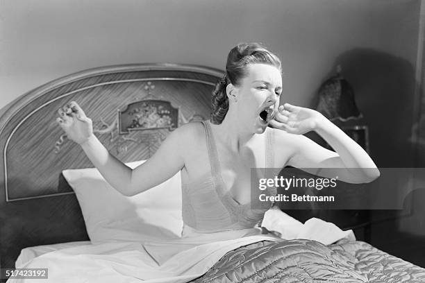 Barbara Lewis, in nightgown, sits up and yawns while in bed. Undated photograph.
