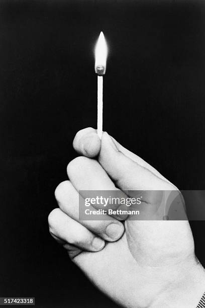 Photo shows a hand holding a lit match on a black background. Undated.