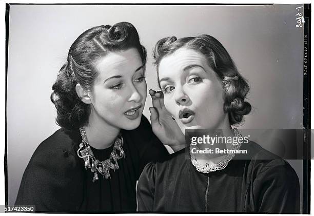 Woman reacts with interest and surprise as another woman whispers in her ear. Undated photograph.
