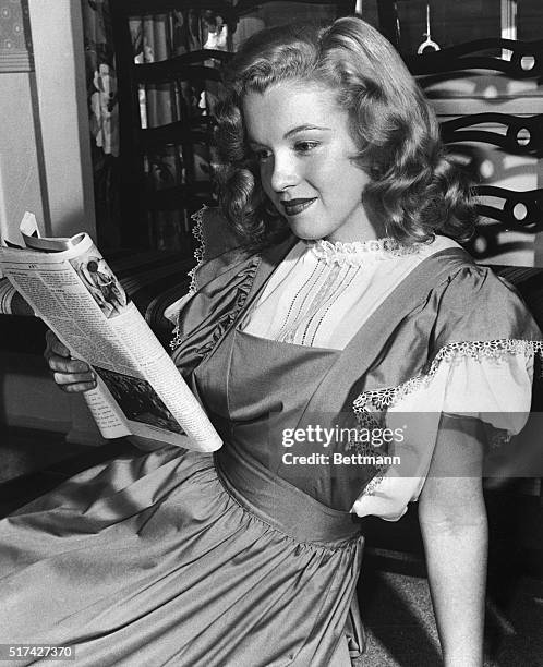 Marilyn Monroe at 21, reading a magazine and wearing a demure dress. Her hair is still long and undyed.