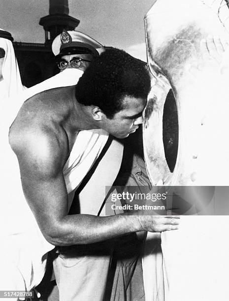 Attired in traditional dress, former world heavyweight boxing champ Muhammad Ali kisses the Holy Black Stone in the Kaaba during his pilgrimage to...