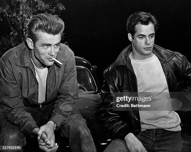 Actor James Dean smokes a cigarette beside another actor in a scene from Rebel Without a Cause.