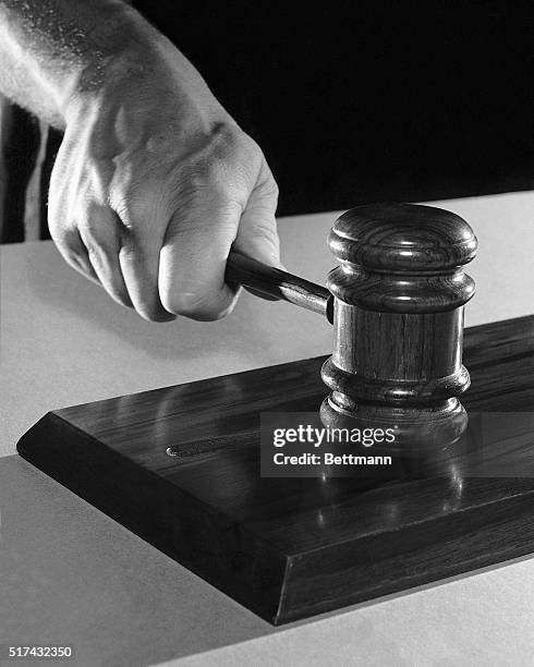 Photo shows a hand holding a gavel, just having banged it on a wooden block. Undated.