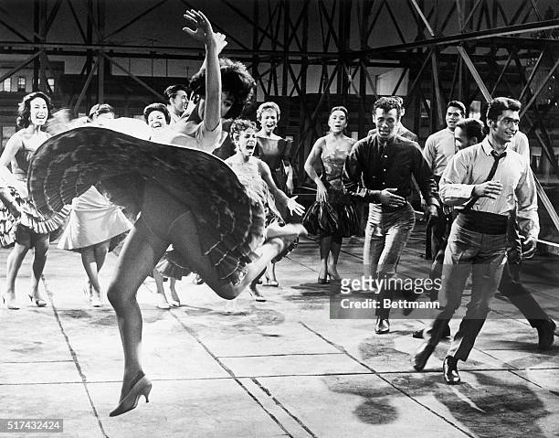 Whirling wildly and kicking up her heels, Rita Moreno, as Anita, dances with members of a Puerto Rican gang and their girlfriends support in a scene...