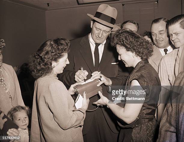 Photo shows actor John Wayne signing autographs for admiring fans after the court decision in his alimony case.