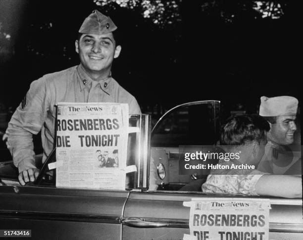 Soldier smiles from the backseat of a convertible as he proudly displays a newspaper announcing the impending executions of Julius and Ethel...