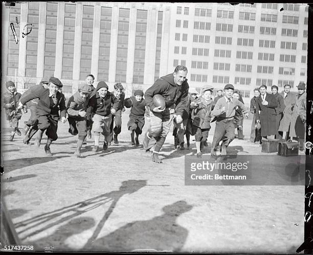 Still a hero to the children, Red Grange the college star, is showing them how to run the ball through the line as he works out with his team, the...