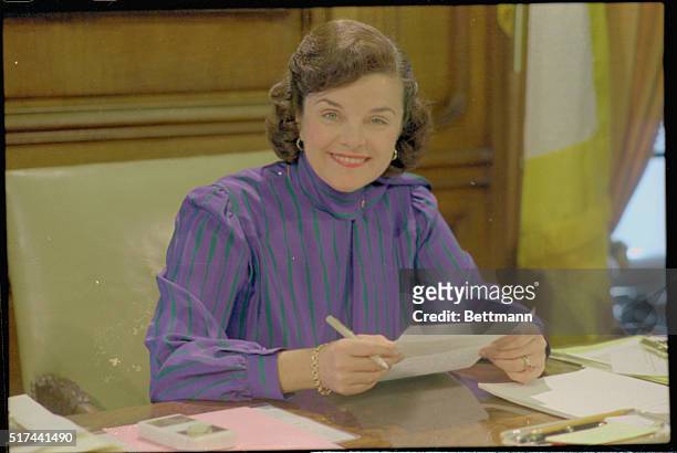 San Francisco's mayor Dianne Feinstein smiling and reviewing a document in her city hall office.