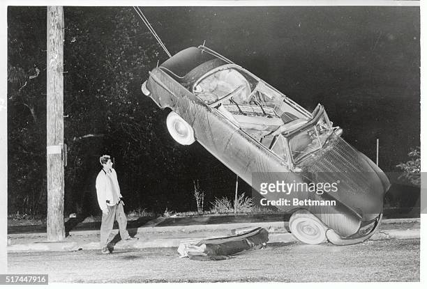 Starke Norris inspects his car, which straddles some telephone pole wires after an unusual accident in Los Angeles. The auto skidded on rain-slicked...