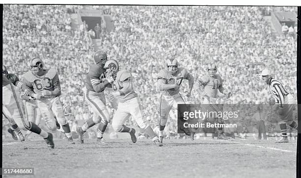 Los Angeles Ram's quarterback Norm Van Brocklin, , who has just handed off to Ron Waller watches him follow the blocking of Duane Putnam around end...