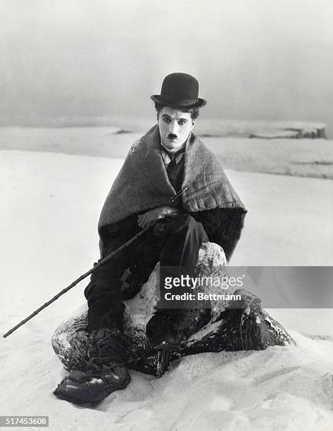 Charlie Chaplin sits wrapped in a blanket in the snow as The Lone Prospector in his 1925 film The Gold Rush.