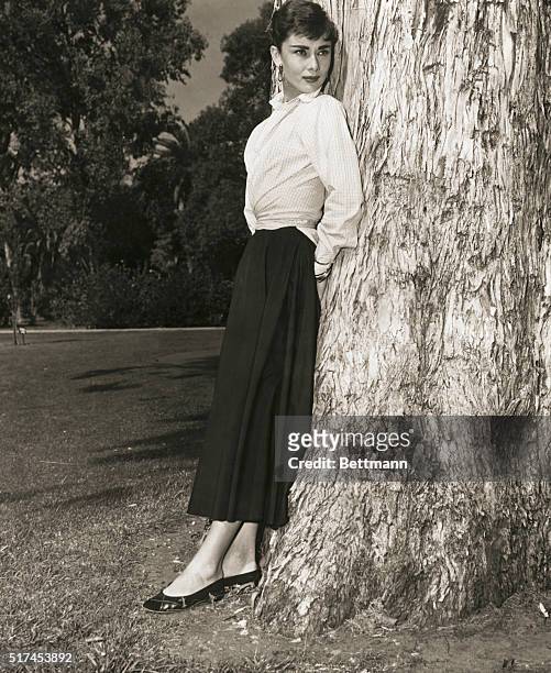 Belgian-born actress, Audrey Hepburn standing against a tree in a publicity photograph circa 1950s.