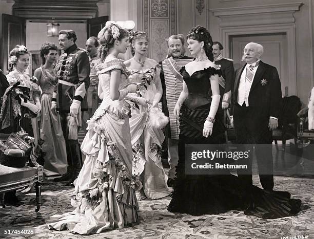 Greta Garbo as Anna Karenina walking down staircase on the arm of husband, Alexei Karenina played by Basil Rathbone. Behind them is a procession of...