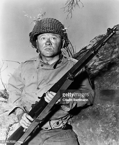 Mickey Rooney is crouching behind huge boulder, holding his rifle in film still from