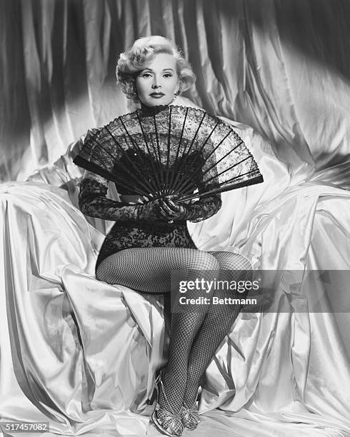 Hungarian actress Zsa Zsa Gabor in fish net stockings holding a lace fan.