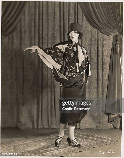 Woman modeling silk scarf blouse with matching knee-length wrap skirt, small brimmed cloche hat and patent leather evening shoes with open lace front...