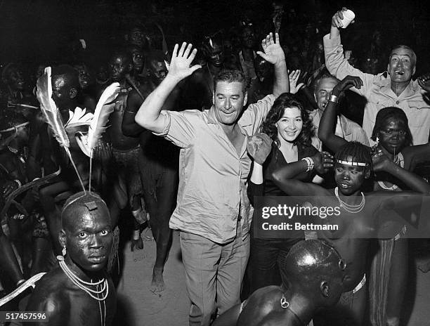 Errol Flynn, Juliet Greco and John Huston happily join a group of African dancers. All three are on location in Africa working on the 1958 film The...