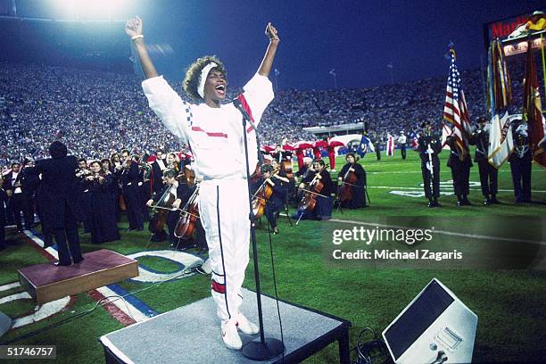 Whitney Houston sings the National Anthem during the pregame show at Super Bowl XXV while tens of thousands of football fans wave tiny American flags...