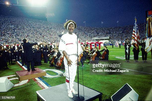 Whitney Houston sings the National Anthem during the pregame show at Super Bowl XXV while tens of thousands of football fans wave tiny American flags...