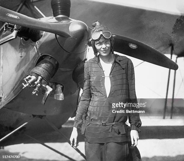 Amelia Earhart stands in front of her airplane.