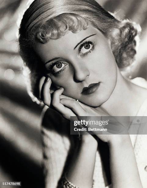 Head and shoulders portrait of Bette Davis with short blonde curled hair, with her head resting on her hands, with a faraway look in her eyes....