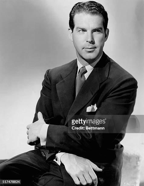 Publicity handout of actor and producer Fred MacMurray . MacMurray sits with his arms crossed over his lap and wears a dark suit and tie.