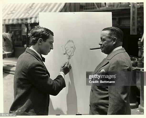 Buster Keaton pretends to work on a drawing actually started by cartoonist George McManus , who poses so as to mimic his character Jiggs from the...