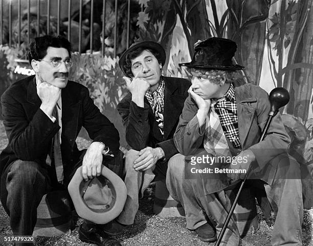 Scene from an unidentified Marx Brothers film, showing Groucho, Chico, and Harpo sitting down on buckets, resting their fists under their chins.