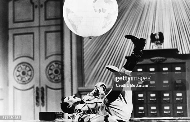 Actor and director Charlie Chaplin kicks a globe in the air while lying on a table in a scene from his 1940 film The Great Dictator.