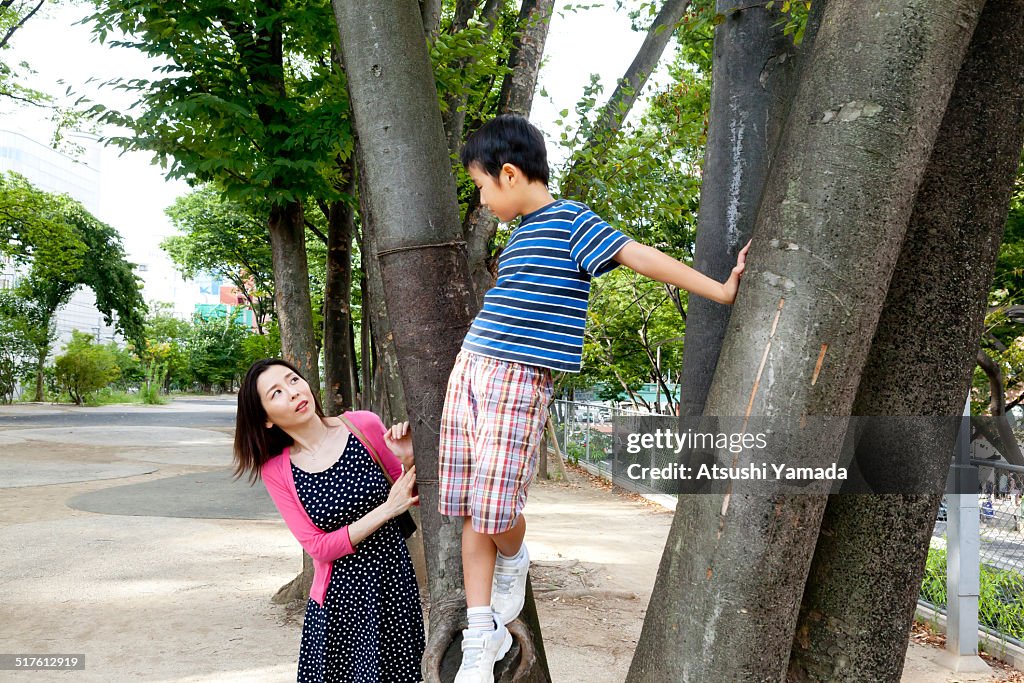 Asian boy climbing tree,talking to mother