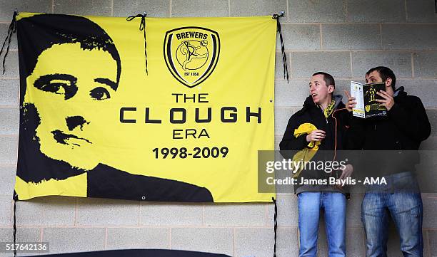 Burton Albion supporters stand next to a flag that says 'The Clough era 1998-2009' before the Sky Bet League One match between Burton Albion and...