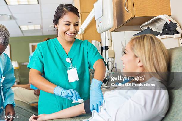 nurse bandaging arm after patient donates blood in hospital bank - donation stock pictures, royalty-free photos & images