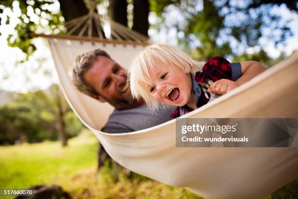 modern dad hugs his blond child on hammock in garden - hammock stock pictures, royalty-free photos & images