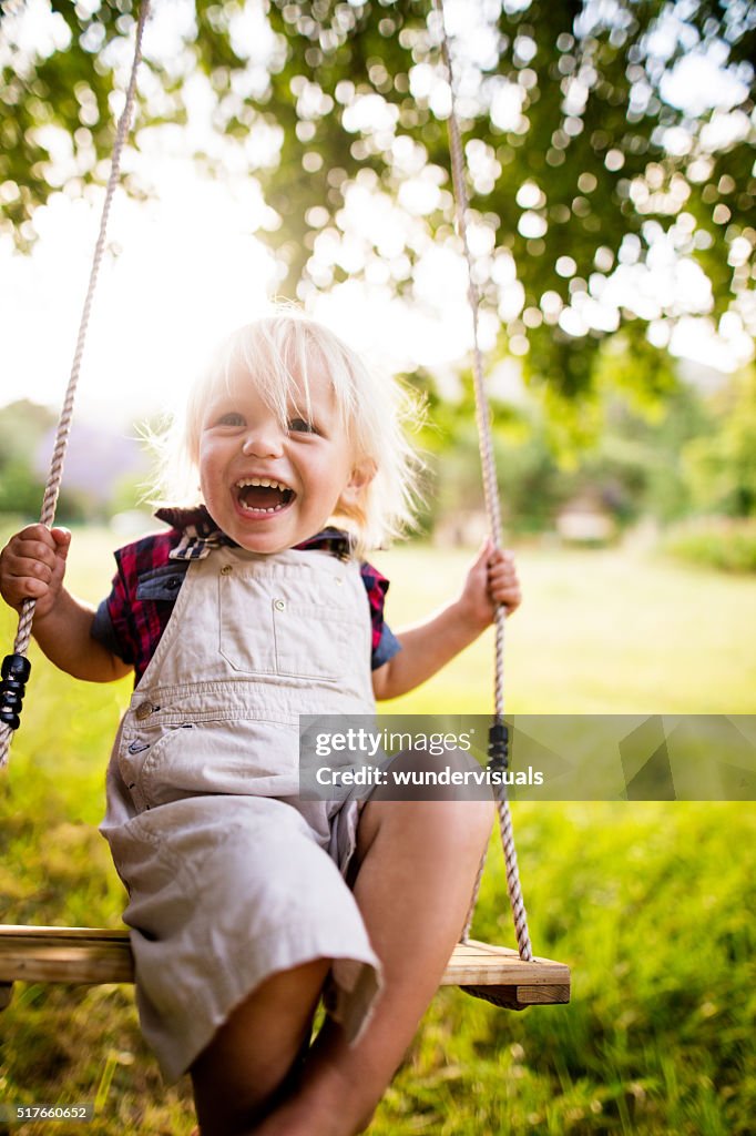 Schurkisch Kind Lachen im Freien auf Schaukel ein Sonnenuntergang im Garten