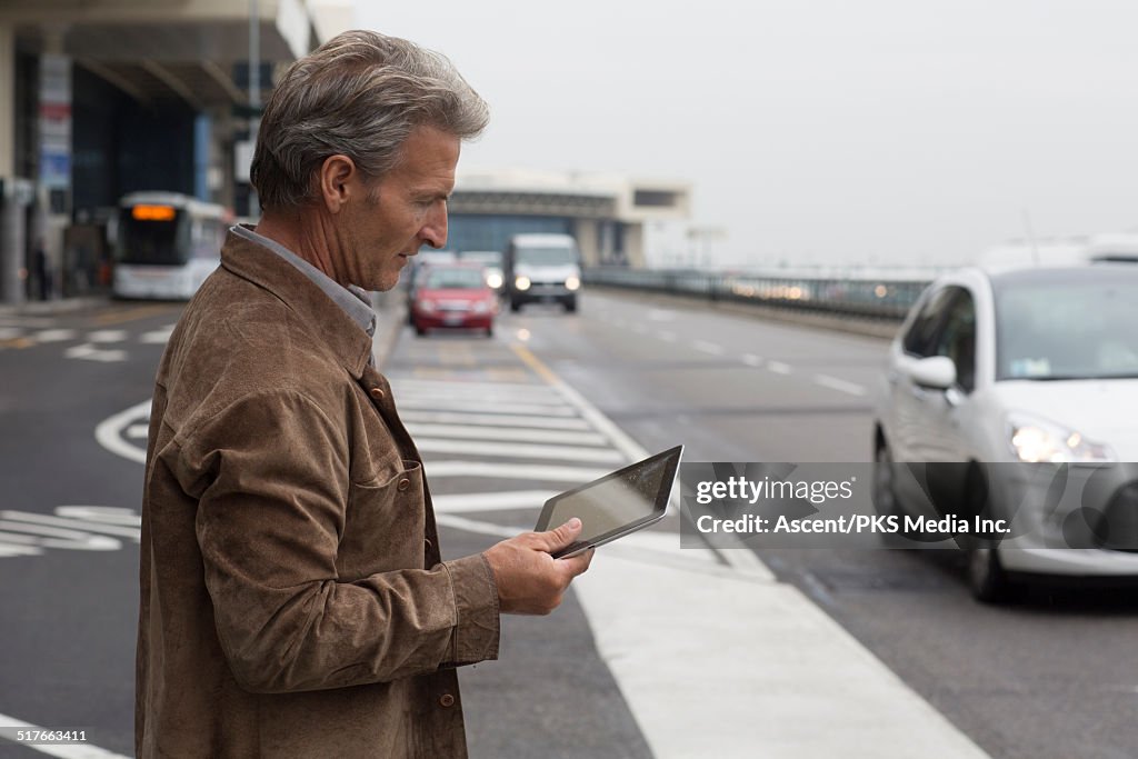 Businessman looks at tablet while waiting for taxi