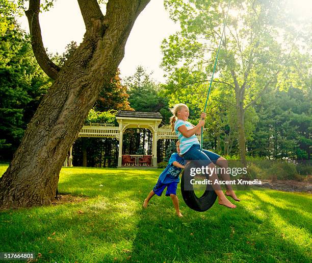 boy pushes girl on backyard swing, meadow - tire swing stock pictures, royalty-free photos & images