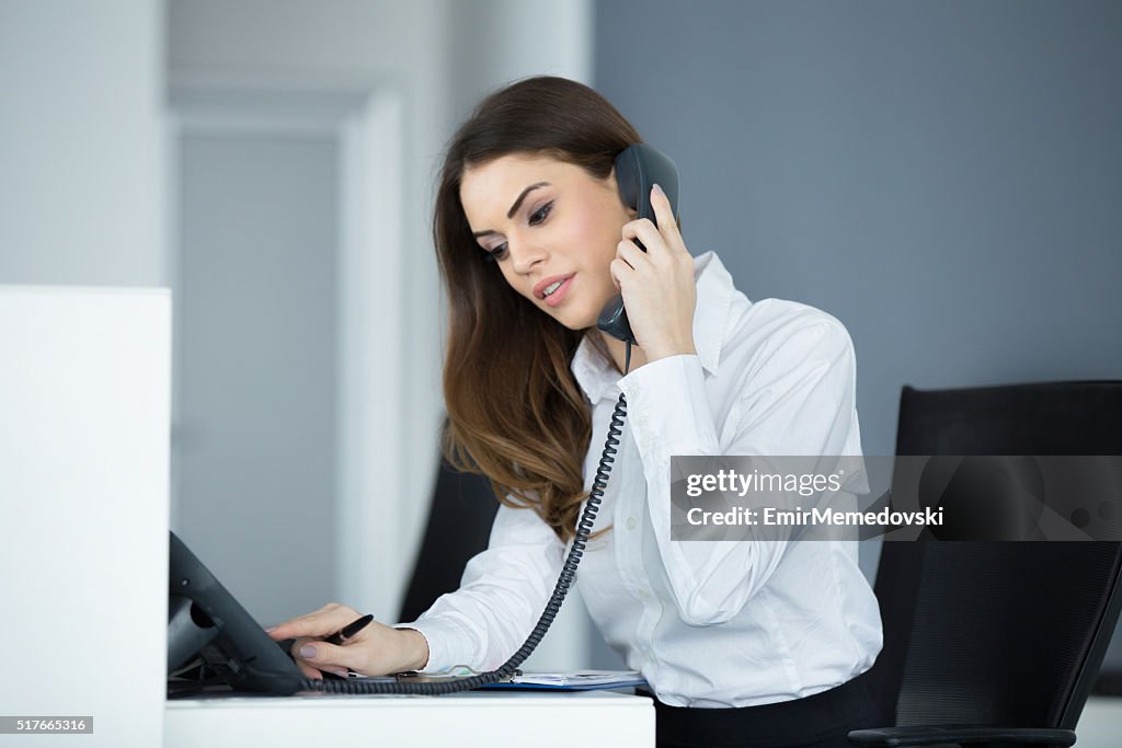 Young smiling secretary communicating over the phone.