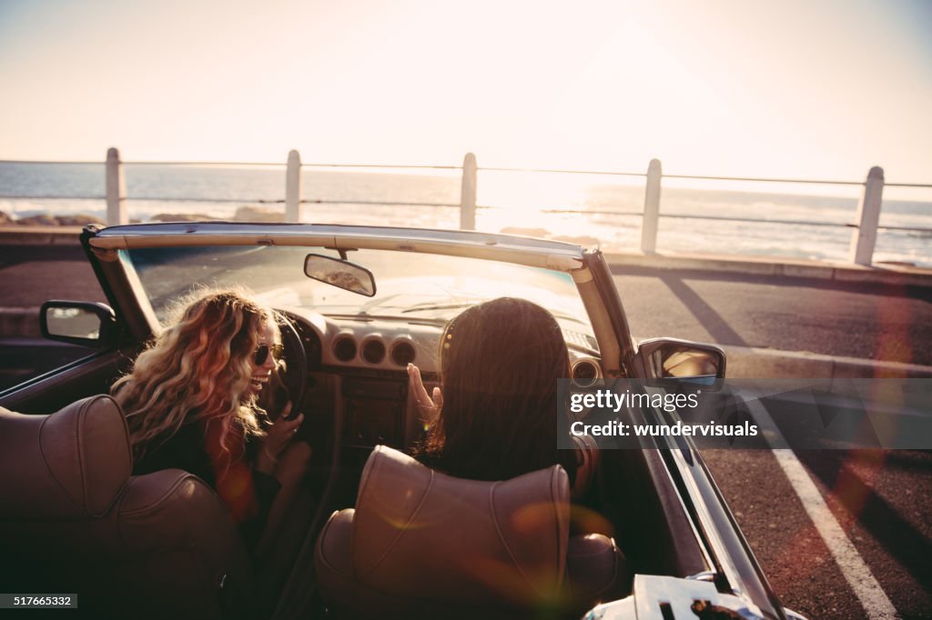 Happy female friends cheering in a convertible at sunset