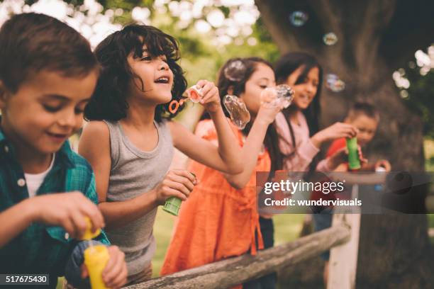 little boy having fun with friends in park blowing bubbles - bellenblaas stockfoto's en -beelden