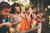 Little boy having fun with friends in park blowing bubbles