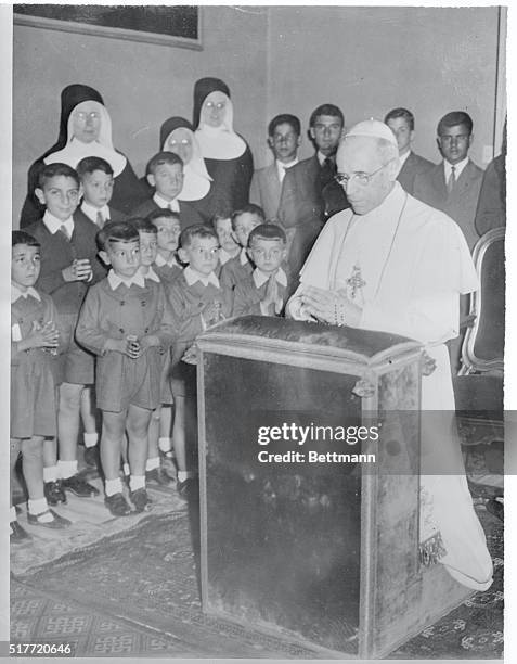 Watched by orphan children from the Villa Nazareth Orphanage in Rome, Pope Pius XII kneels in prayer during a service in his private chapel at his...