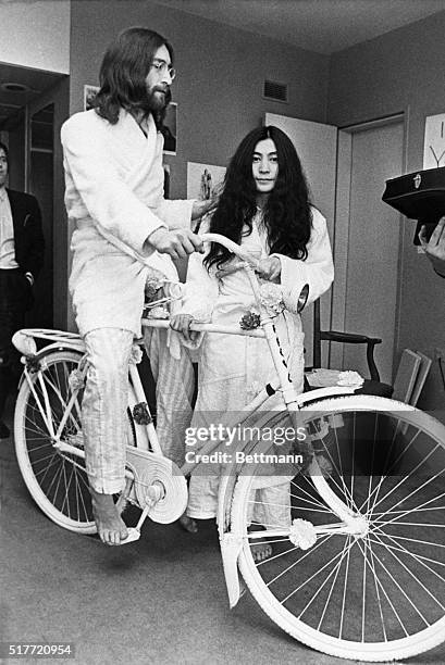 Married musicians John Lennon & Yoko Ono pose with a bicycle the former received as a gift. The couple are in pajamas and robes because they are...