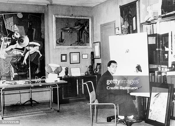Salvador Dali, Spanish Surrealist painter is shown seated in his studio by a work-in-progress, looking at the photographer.