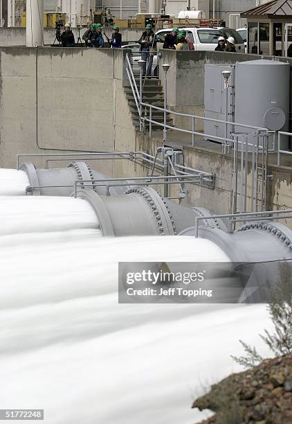 Members of the media and dam operators watch water flow from the bypass tubes of Glen Canyon Dam at a rate of approximately 32,000 cubic feet per...