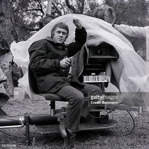 Steve McQueen takes cover as the rains return to Southern California and deluge the Placerita Canyon location site where the actor is starring in the...