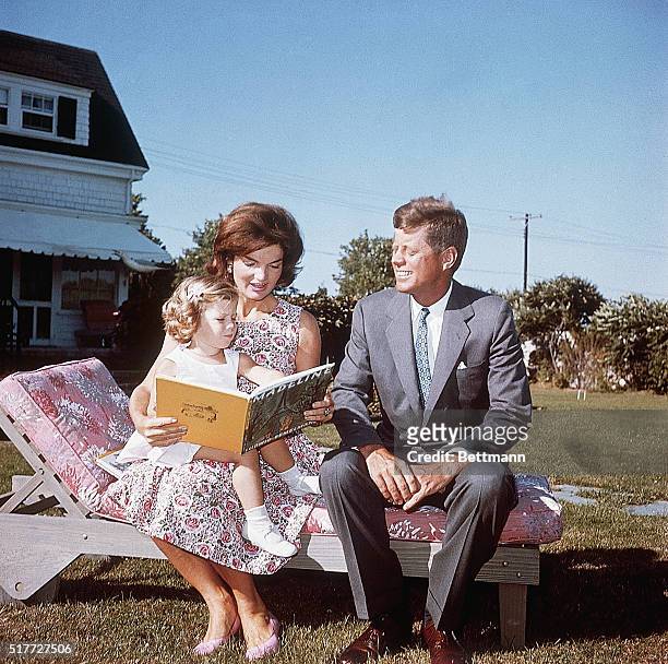 Jacqueline Kennedy and her husband Senator John F. Kennedy sit on a lounge chair at their summer home. Jacqueline reads to her daughter Caroline from...