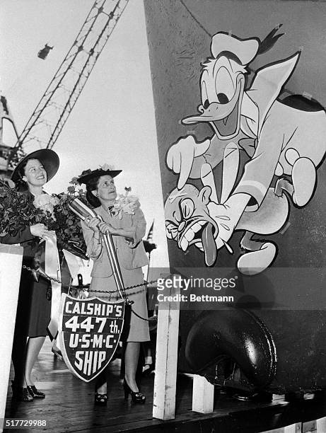 Donald Duck shows Mrs. Walt Disney the best place to aim as she christens the S.S. Rice Victory. Mrs. Spencer Tracy, , the matron of honor, looks on...