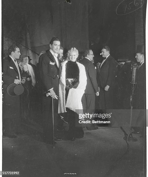 Hollywood California: Miss Thelma Todd with her husband. Miss Todd wore a striking black velvet gown with white ermine coat.