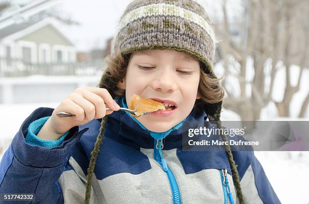 young boy eating maple syrup taffy outside - sugar shack stockfoto's en -beelden